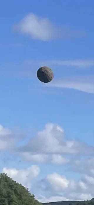 A close up shot of a sphere floating in mid-air, it's noticeably textured and has a greyish colour, sort of looks like some barren moon